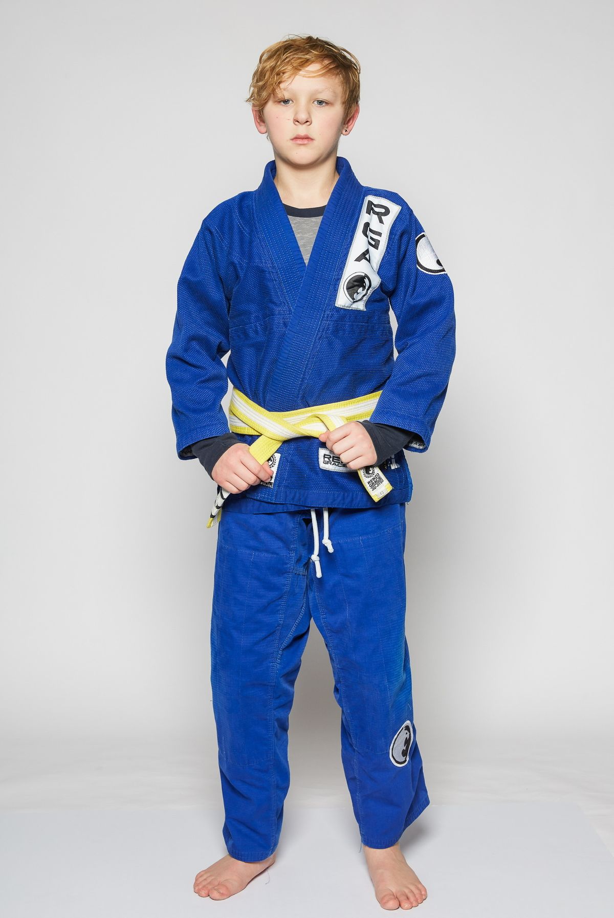 Young Renzo Gracie Milford student standing in a blue gi with a yellow and white belt