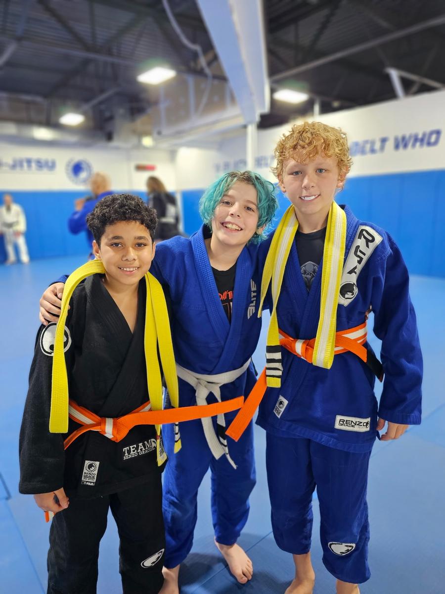 Three kids smiling with their new belts on the mat at Renzo Gracie Milford